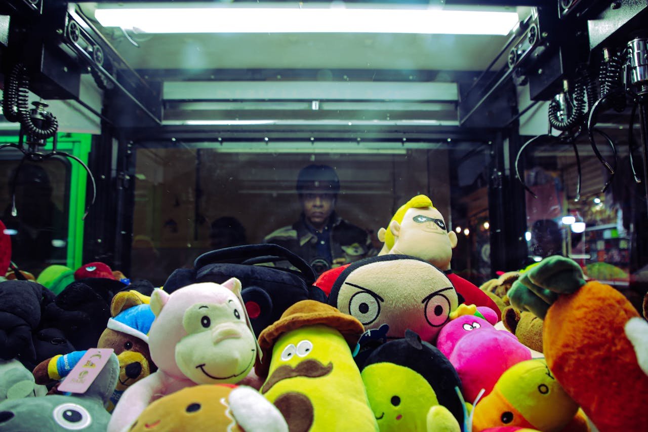 Vibrant plush toys inside a claw machine with a person reflected in the glass.